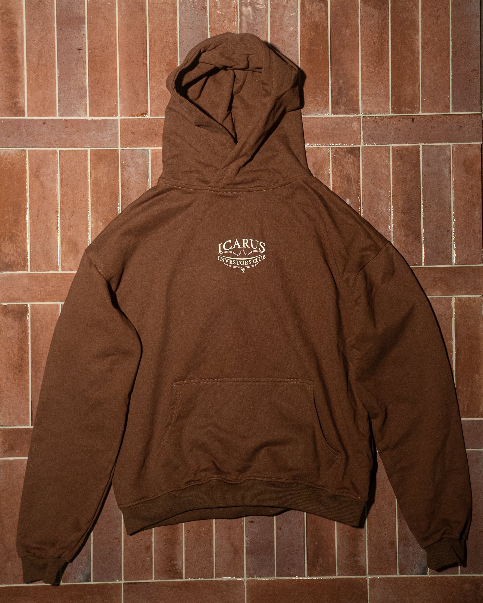 Brown hoodie with a logo on the back against a brown tiled wall