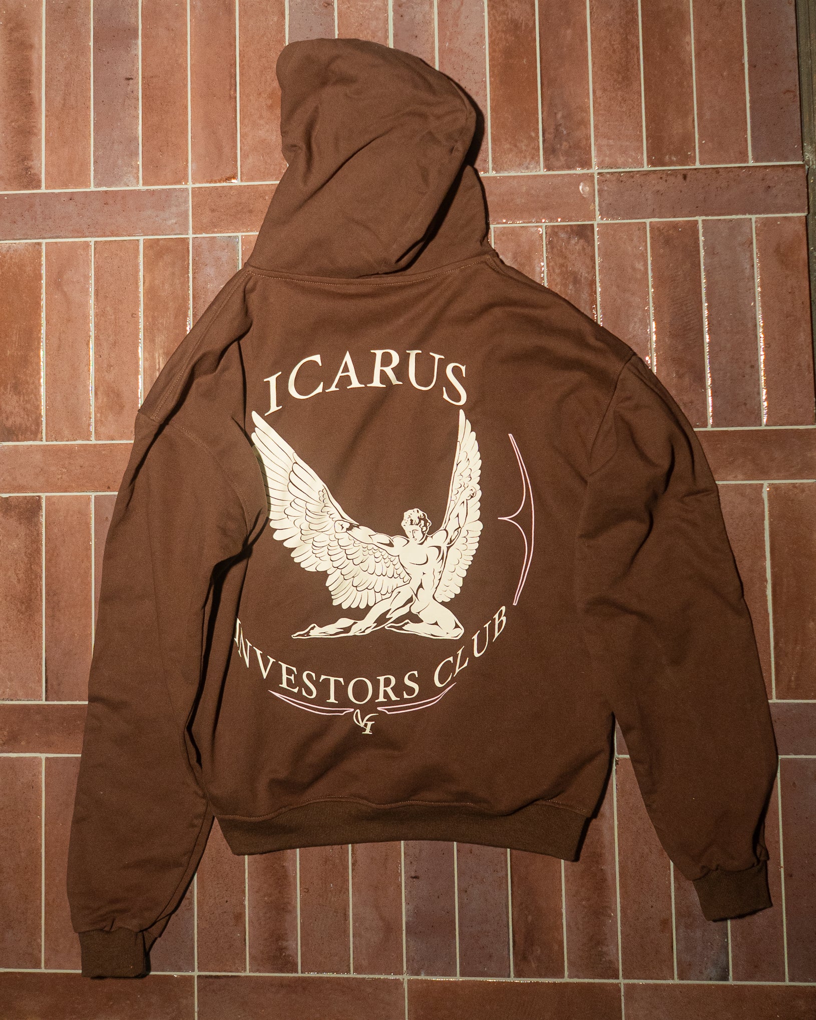 Brown hoodie with 'Icarus Investors Club' design on the back against a brown tiled wall.